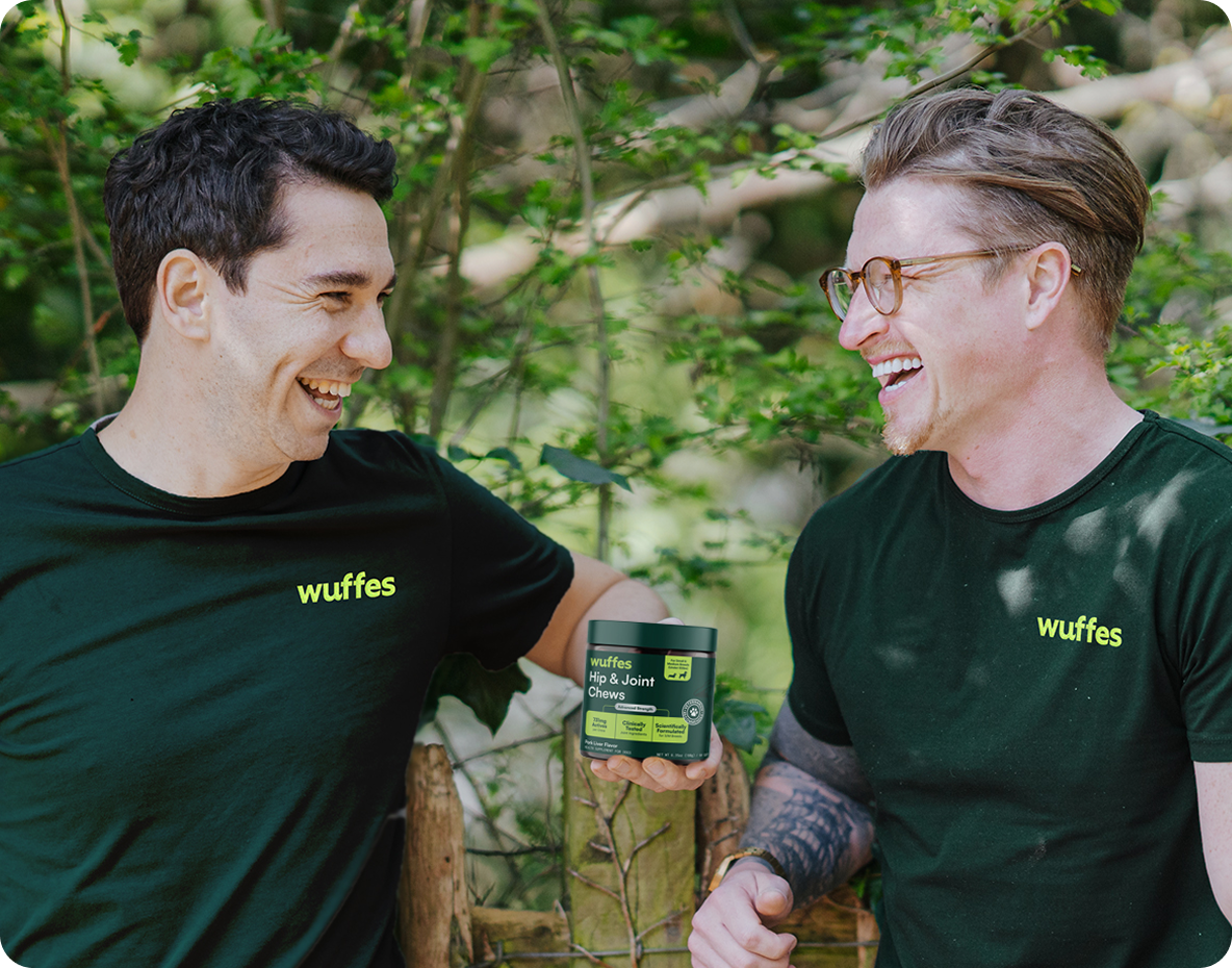 Two men wearing black shirts with wuffes logo holding a container of hip and joint chews outdoors